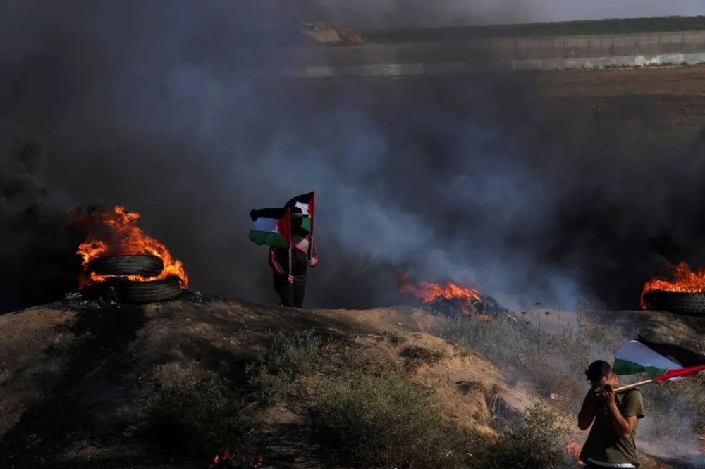 فلسطينيان يرفعان العلم في مواجهة قوات الاحتلال في جنين.