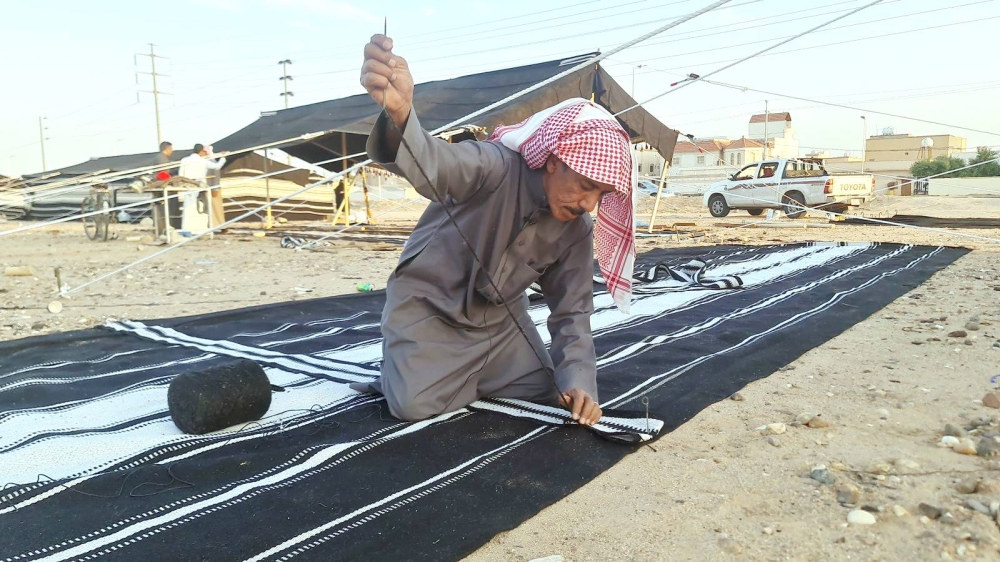 الجميلي يحيك خيمة بعد أن توارث صنعتها. (عكاظ)